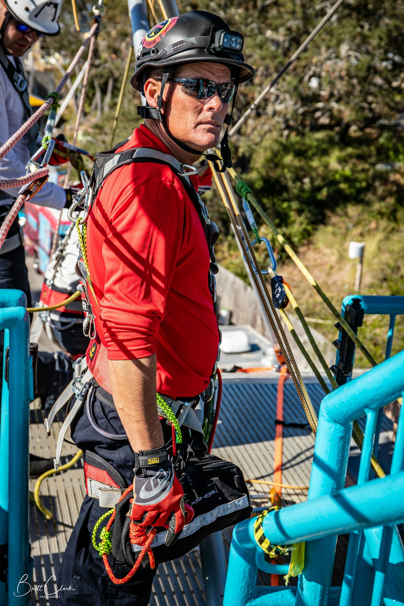 A person in safety gear and a helmet is handling ropes on a blue structure, possibly for climbing or rescue activities.