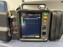 The image shows a medical device, likely a defibrillator or ECG monitor, used for monitoring heart activity.