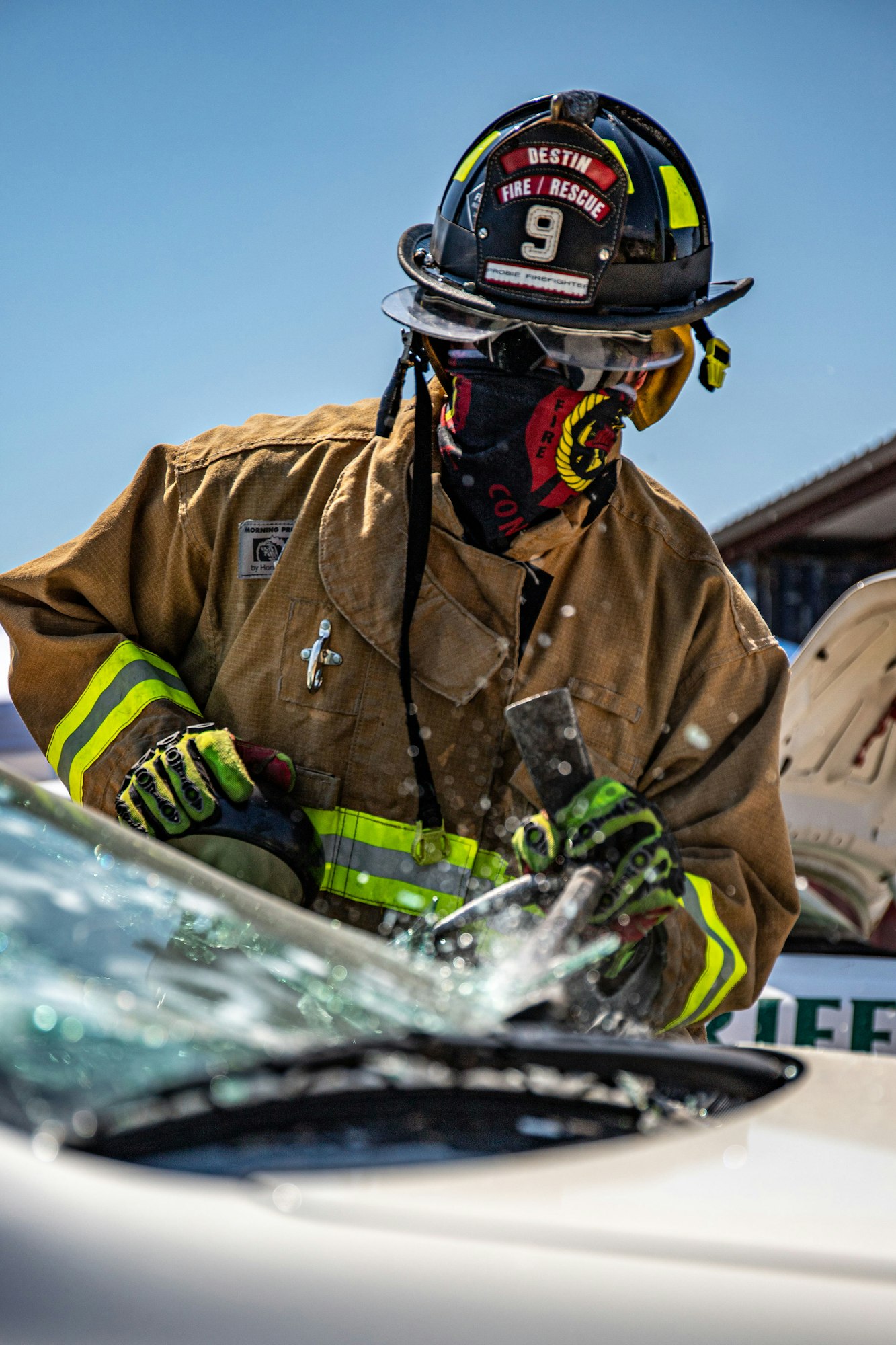 Firefighter in protective gear using a tool to break a car window.