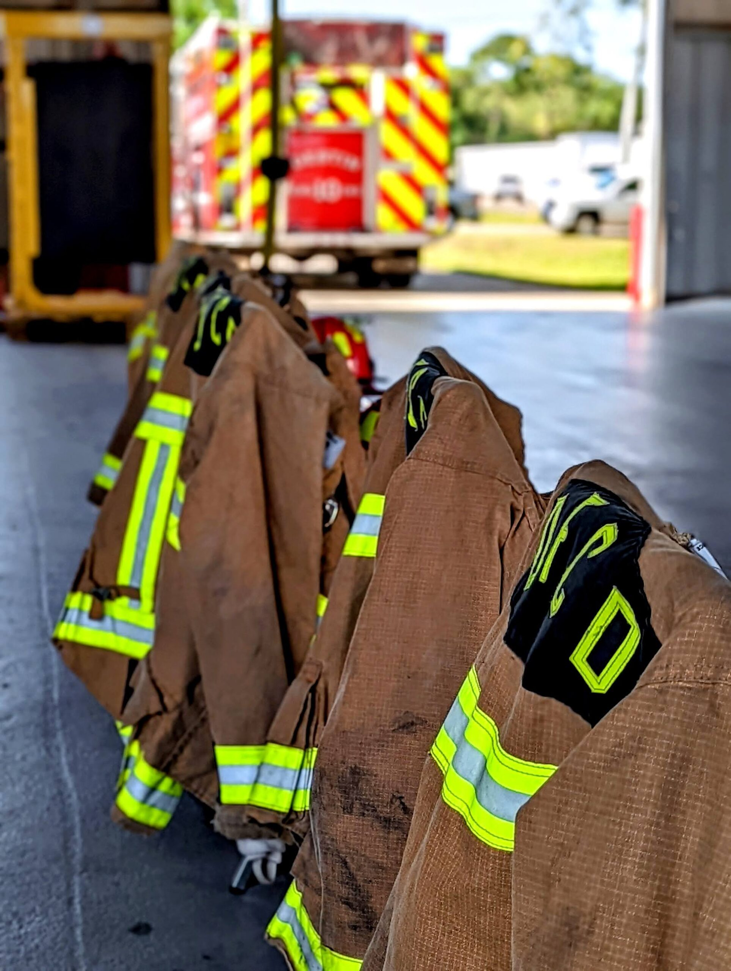 Firefighter jackets hanging in a row, with a blurred fire truck in the background.