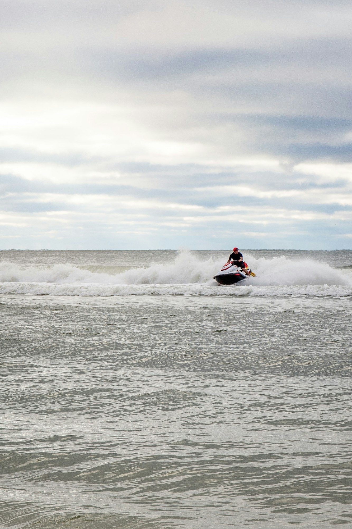Person riding a jet ski on a wavy ocean under a cloudy sky.