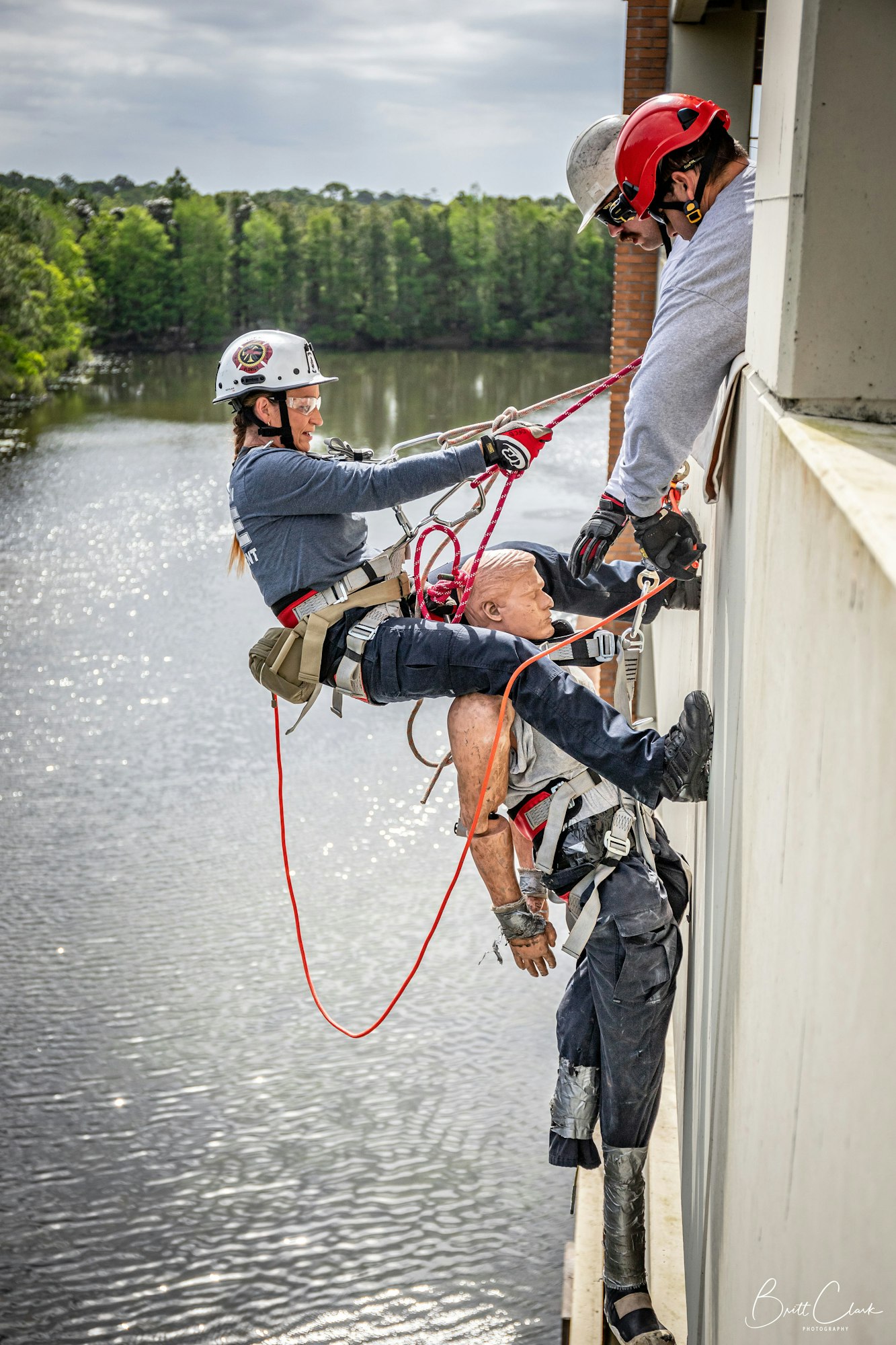 Two people in helmets conduct a dramatic rescue operation, lowering a person with ropes over water.