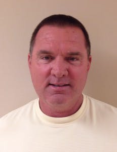 A person with short hair wearing a light-colored shirt, standing against a plain background.