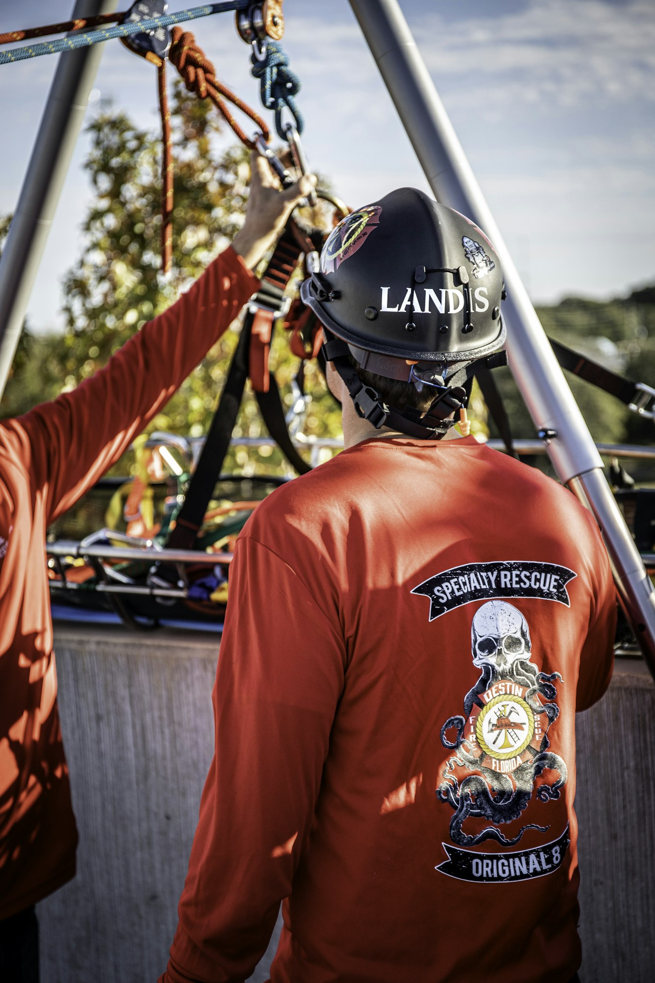 Person in a helmet and red shirt labeled "Specialty Rescue," adjusting ropes on a rescue setup.