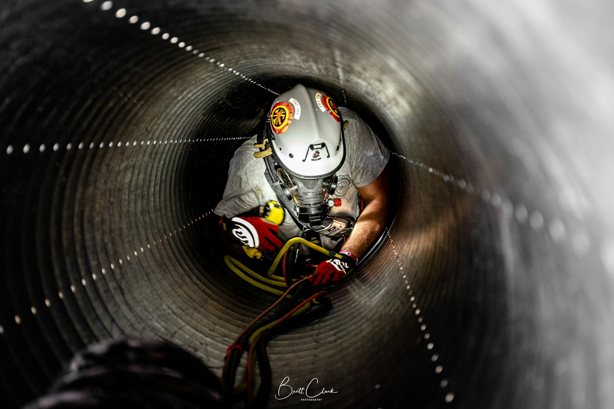 A person wearing safety gear is crawling through a pipe, holding onto a rope.