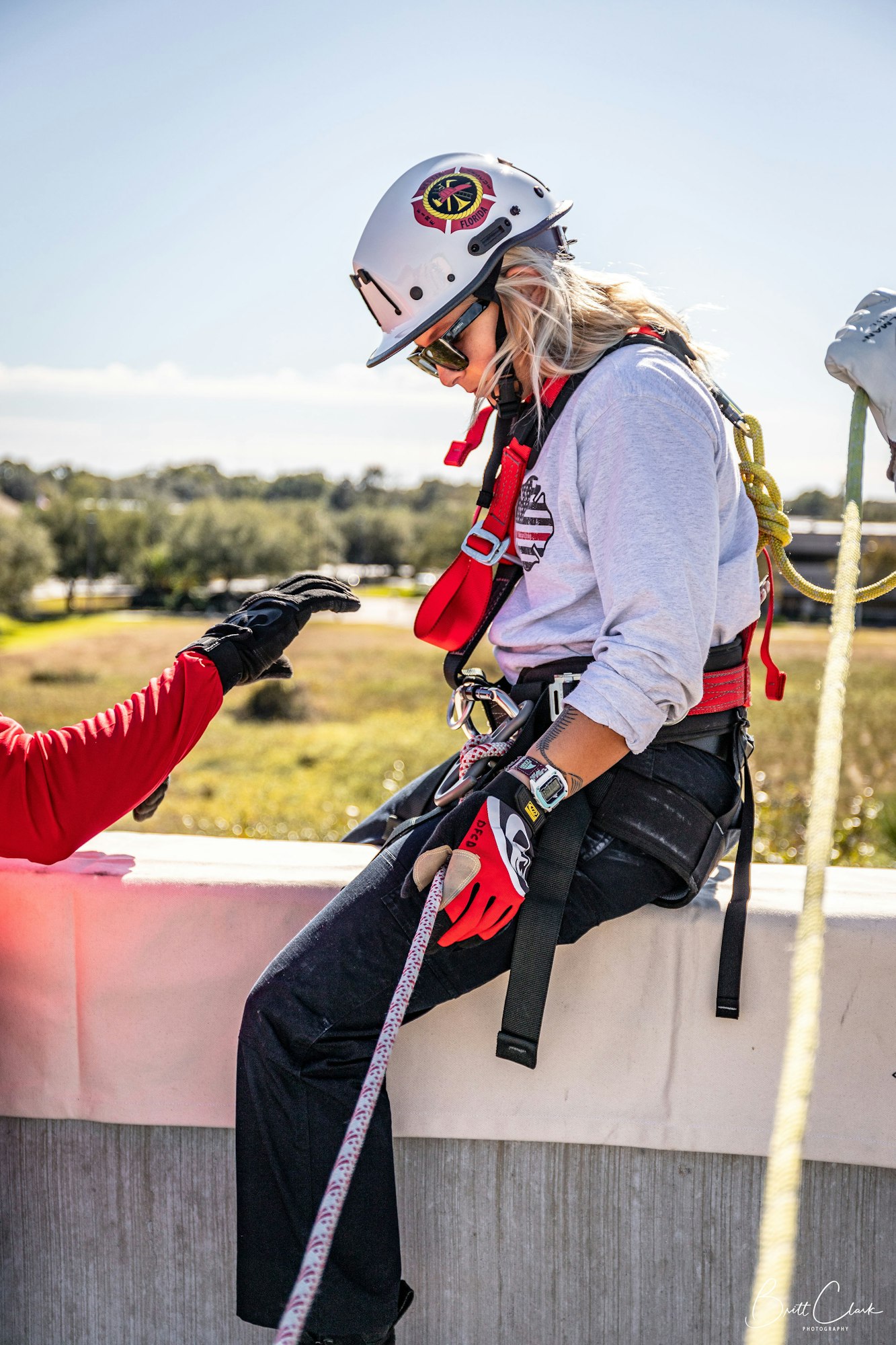 Woman in safety gear, helmet and harness, at height with ropes, assisted by another person.