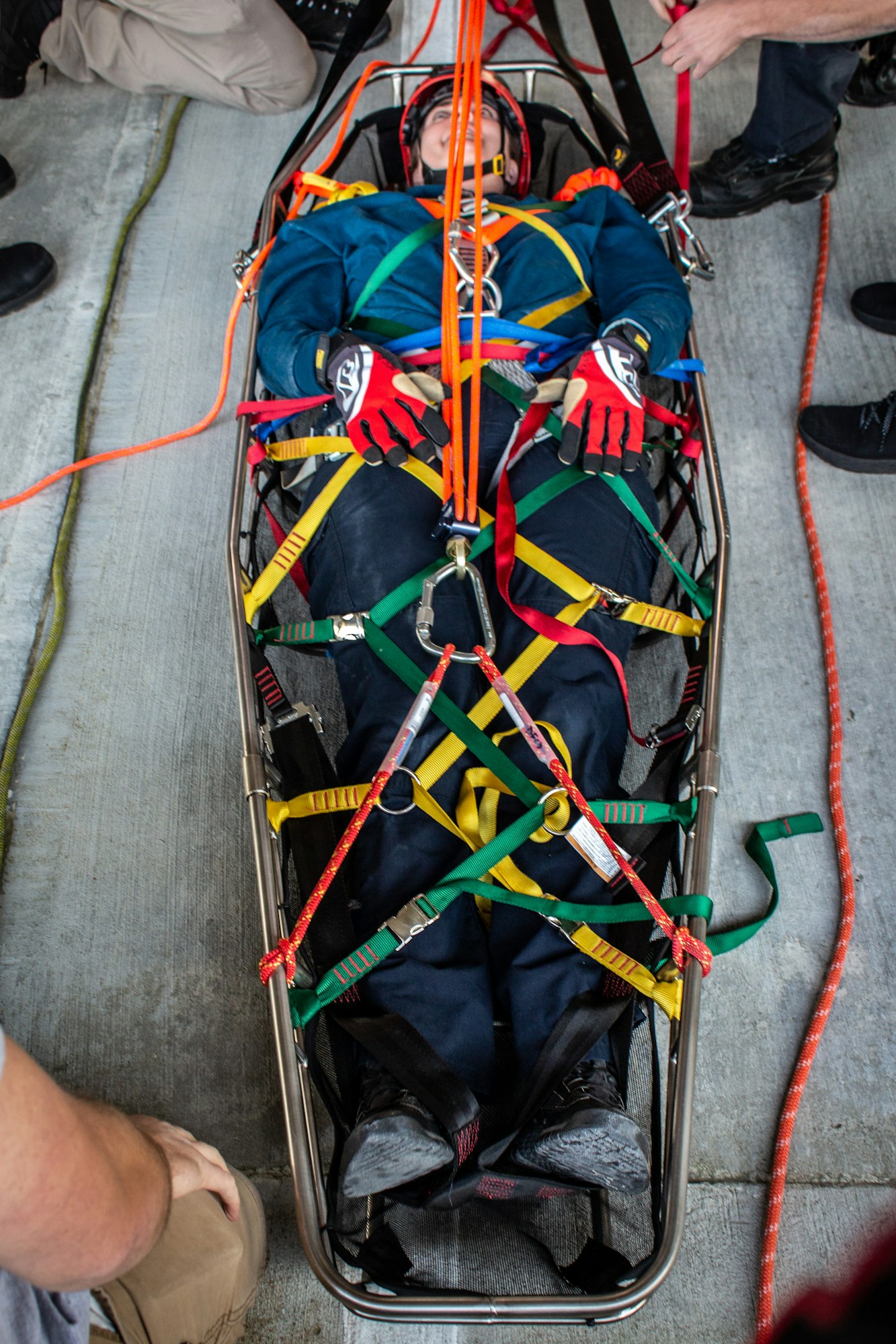 Person in rescue gear secured in a stretcher with multiple colored straps.