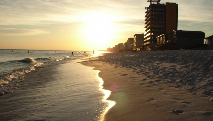Beach at sunset with buildings, people, and calm waves.