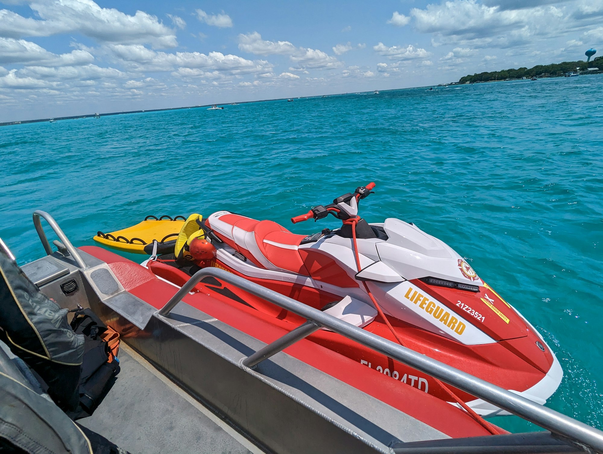 A lifeguard jet ski is docked next to a boat on clear blue water under a partly cloudy sky.