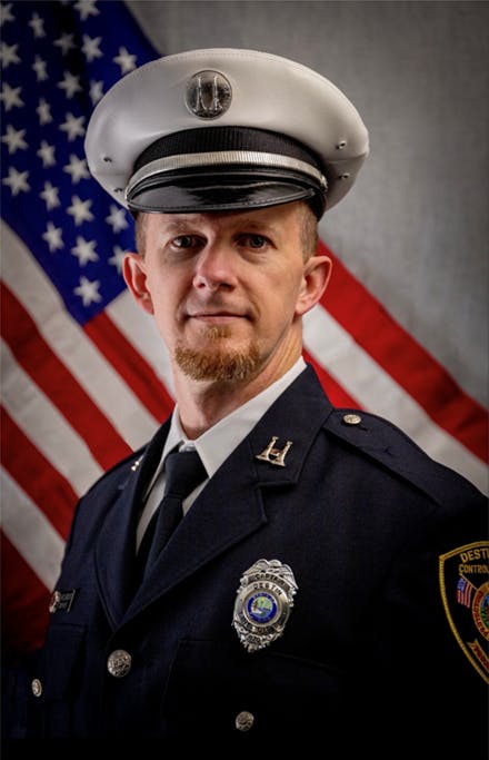 A uniformed officer stands in front of a U.S. flag.