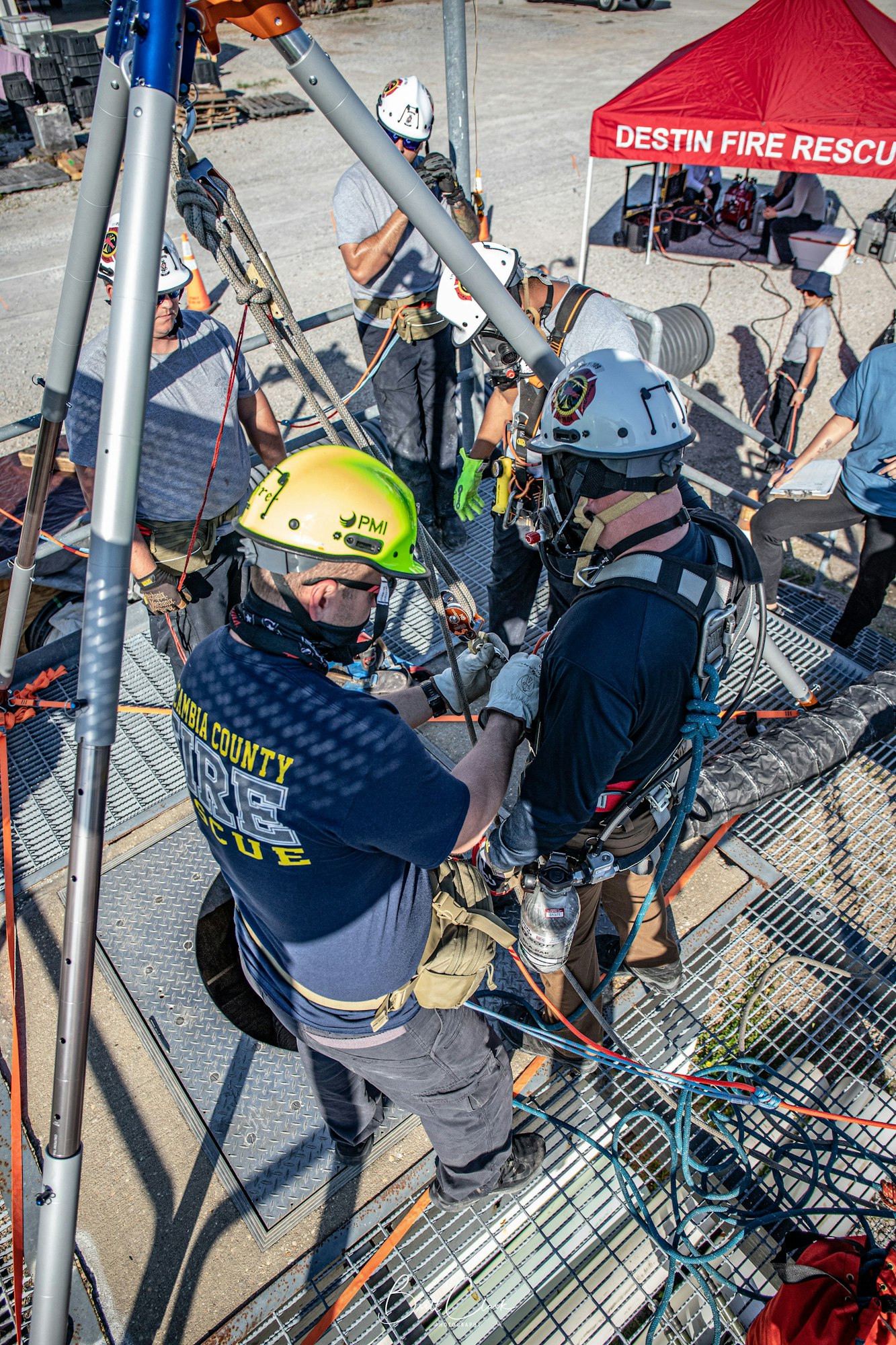 Rescue team conducting a confined space drill with safety gear, ropes, and support under a rescue tent.