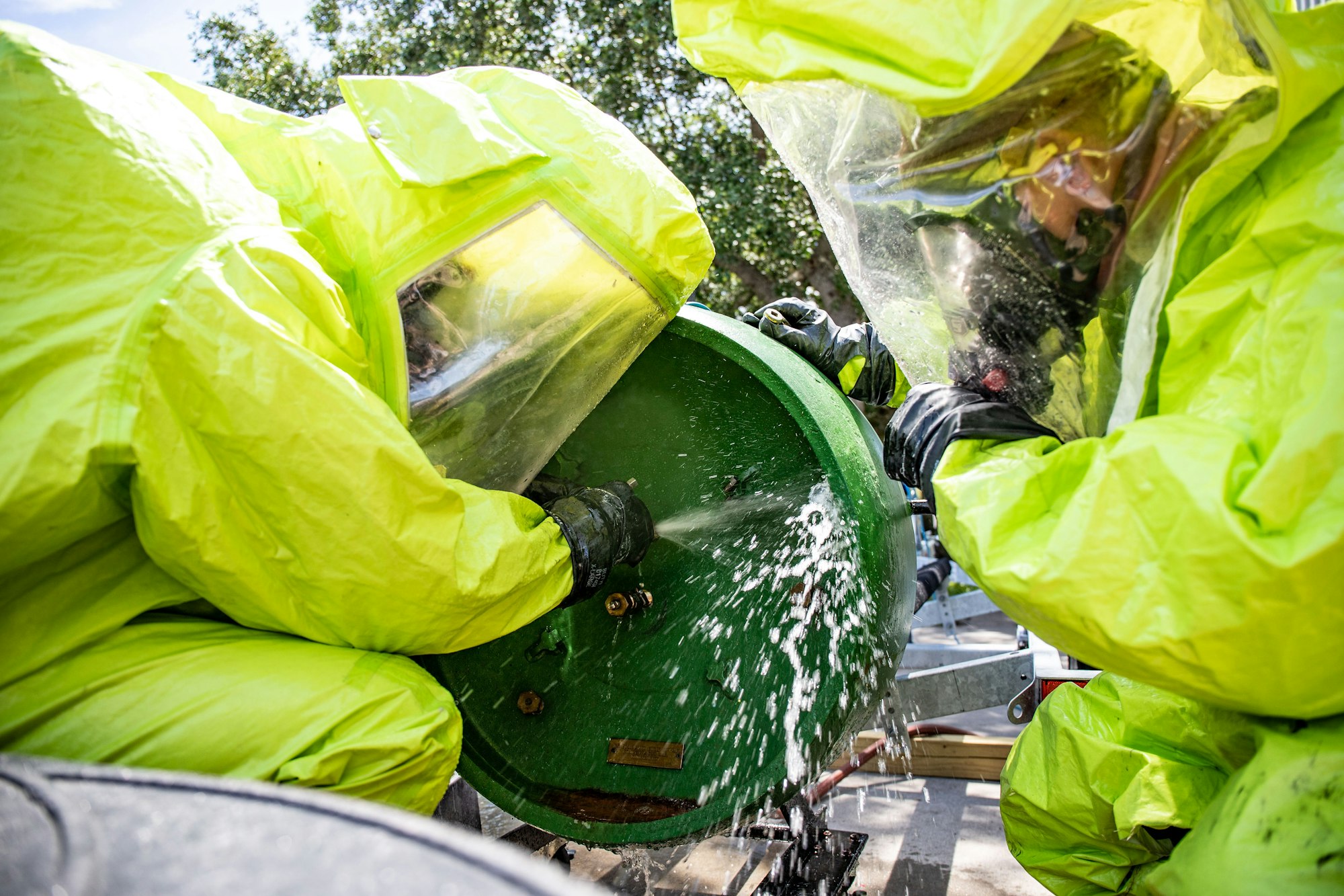 People in hazmat suits handling a spraying green barrel.