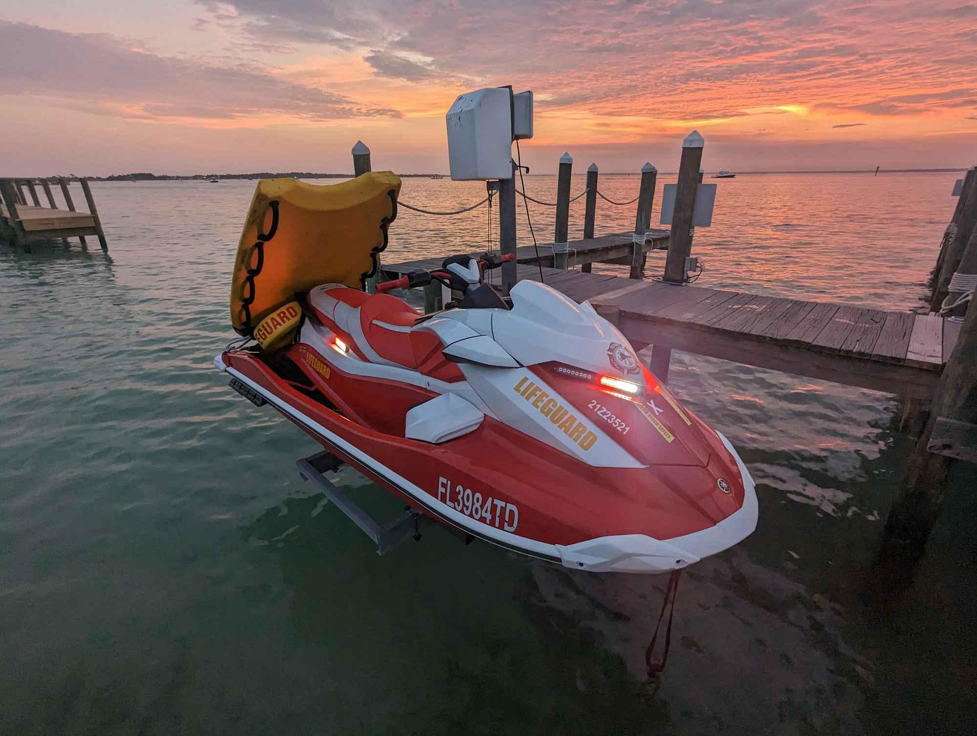Lifeguard jet ski docked at sunset, with a rescue board attached.