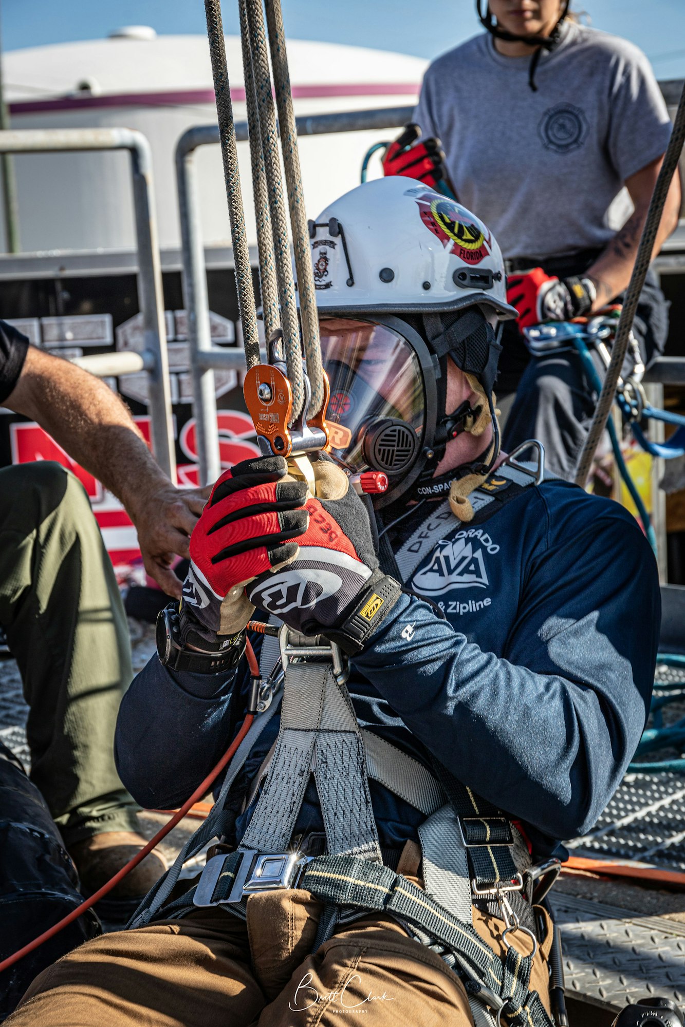A person in safety gear and helmet, holding ropes, appears to be involved in an outdoor rescue or climbing activity.