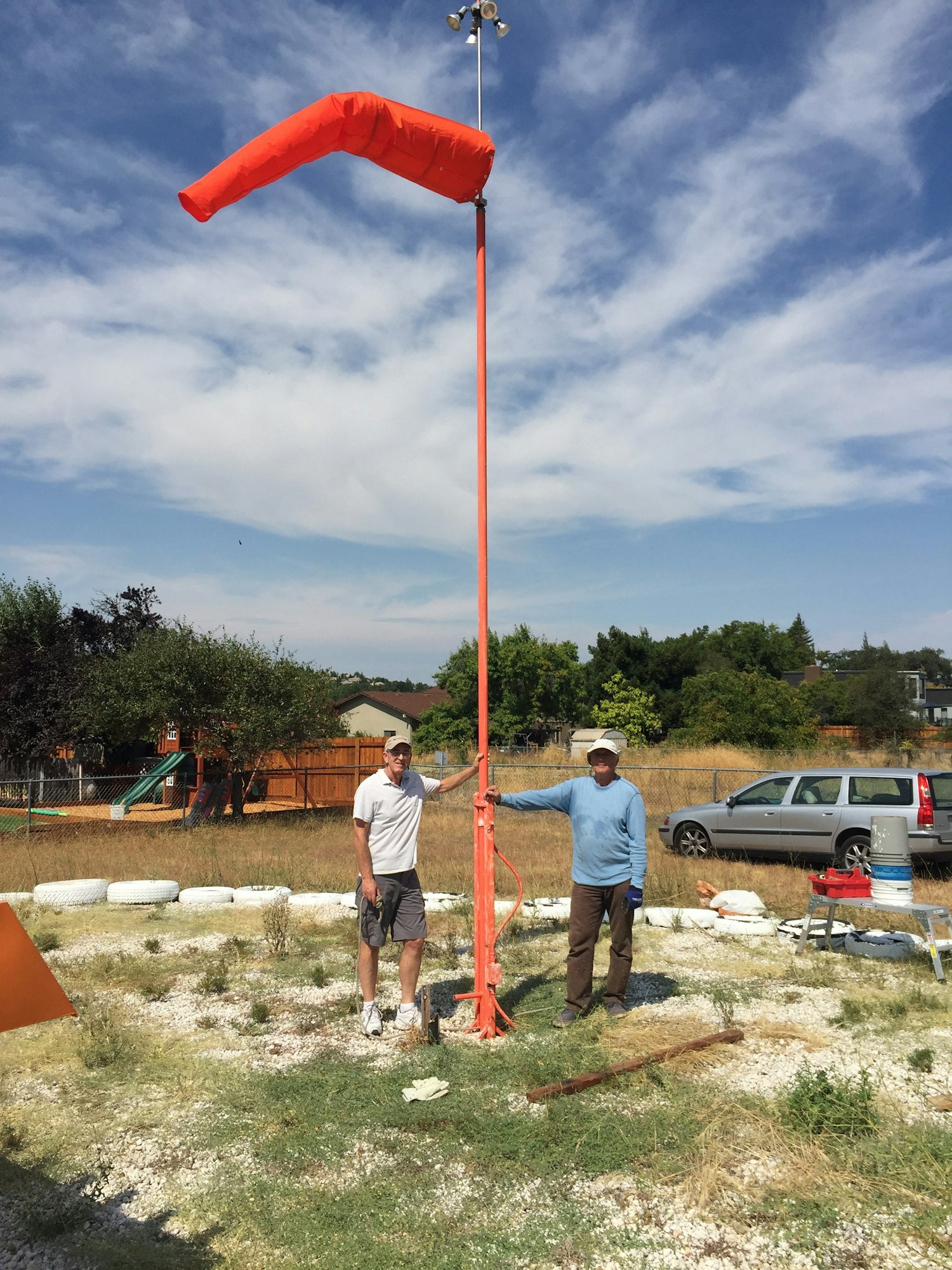 Two volunteers standing at base of flag pole where they installed a new wind sock