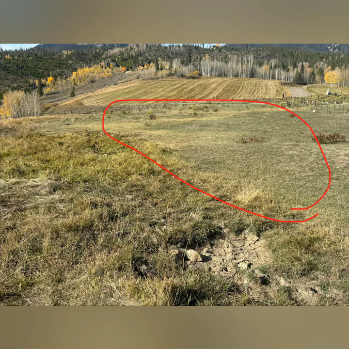 The image shows a grassy field bordered by trees and hills, with a faint marking highlighted in red.