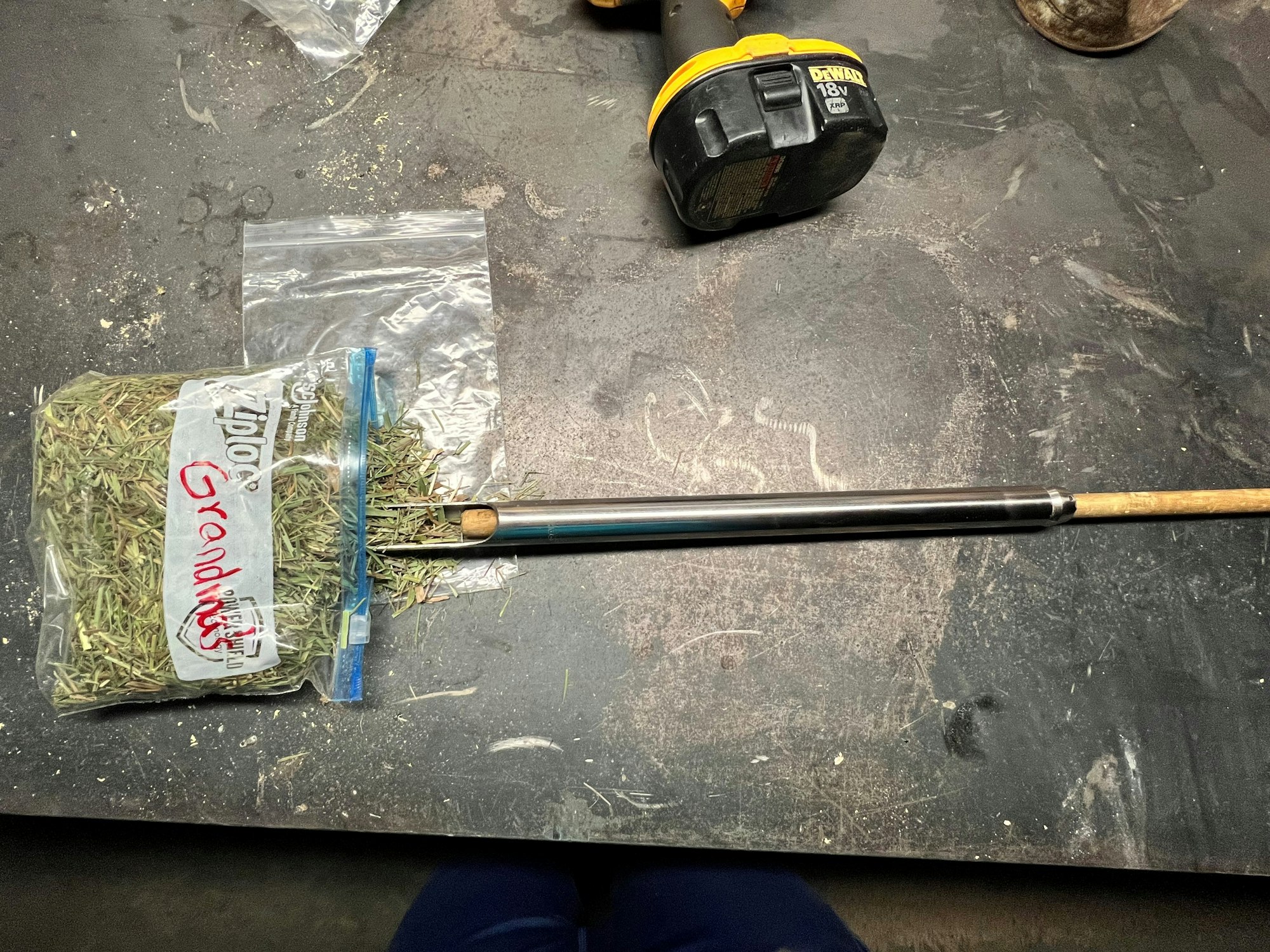 A bag labeled "Granddaddy" with dried plant material, a battery, and a tool on a workbench.