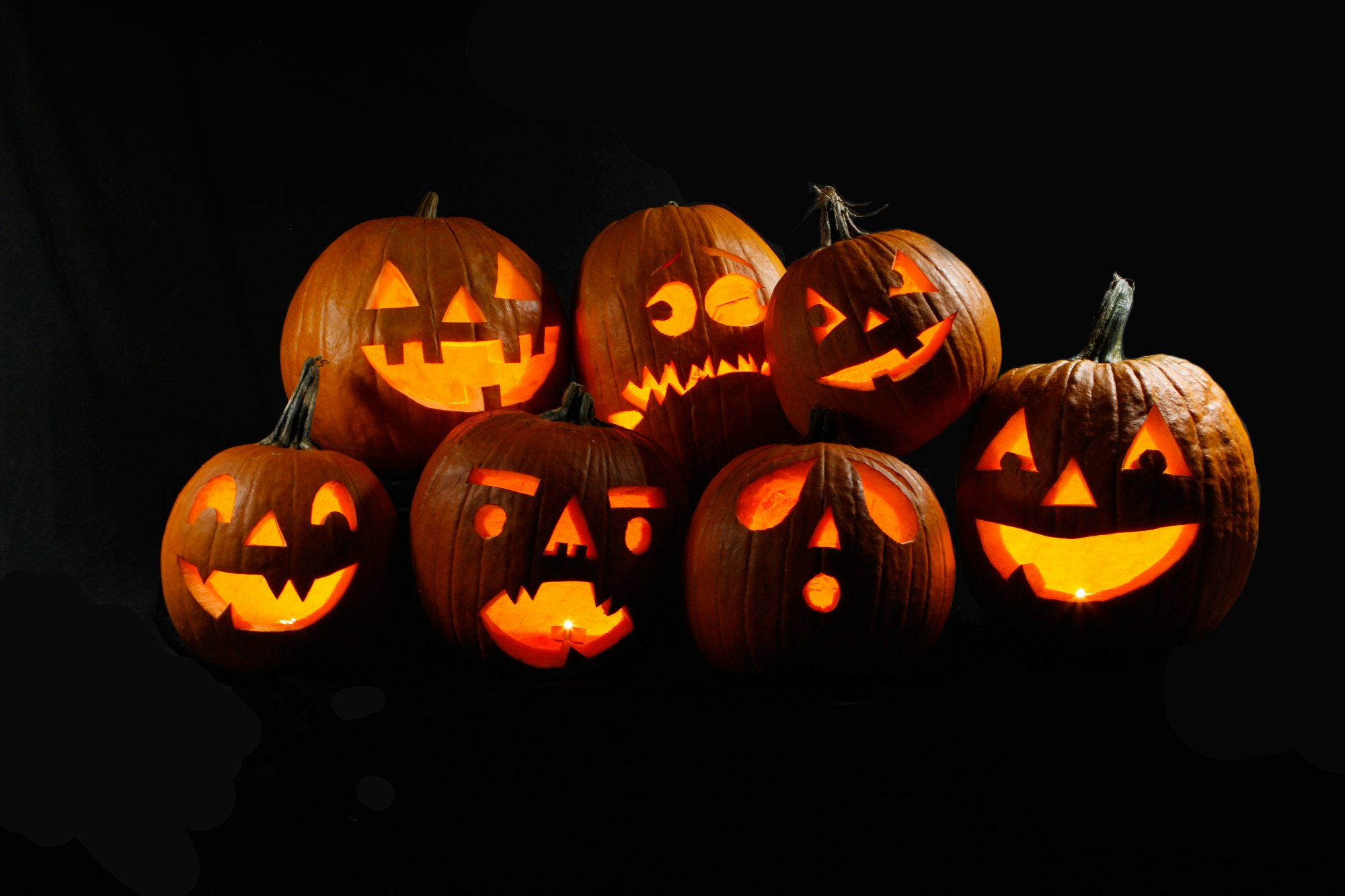 Seven jack-o'-lanterns with various carved faces glowing in the dark.