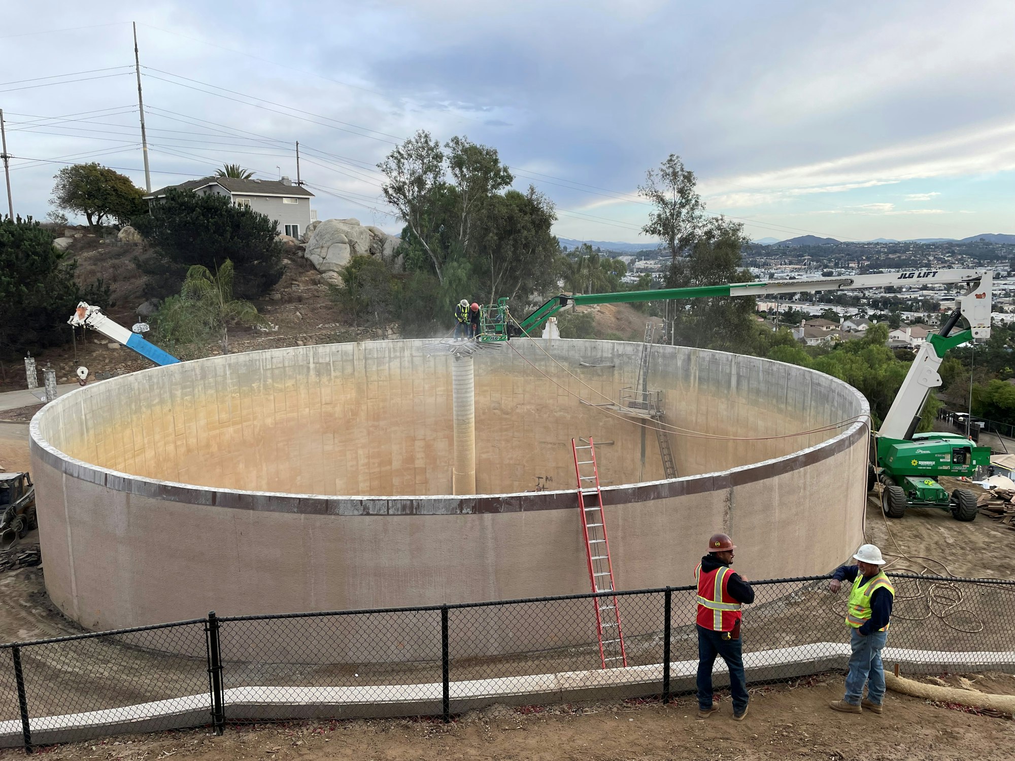 Construction workers near a large circular tank, with cranes and equipment around.