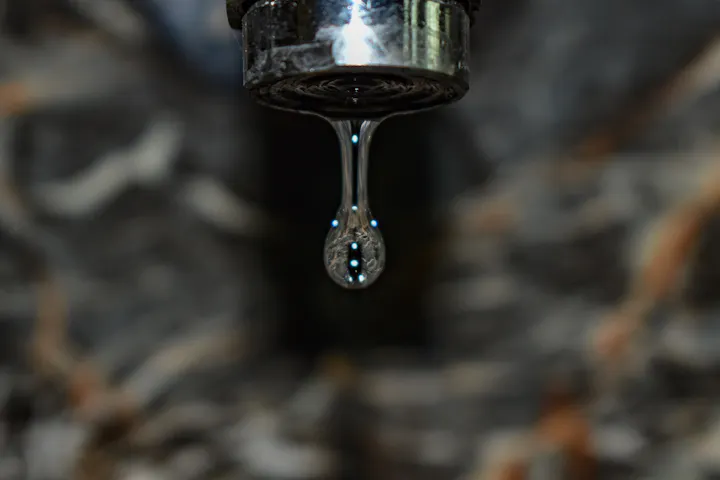 The image features a close-up of a water droplet hanging from a faucet, showcasing intricate details and reflections.