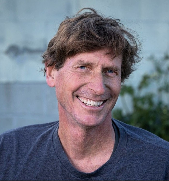 A person smiling outdoors, wearing a gray shirt.