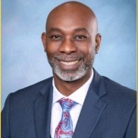 A person in a suit and tie, smiling against a light blue background.