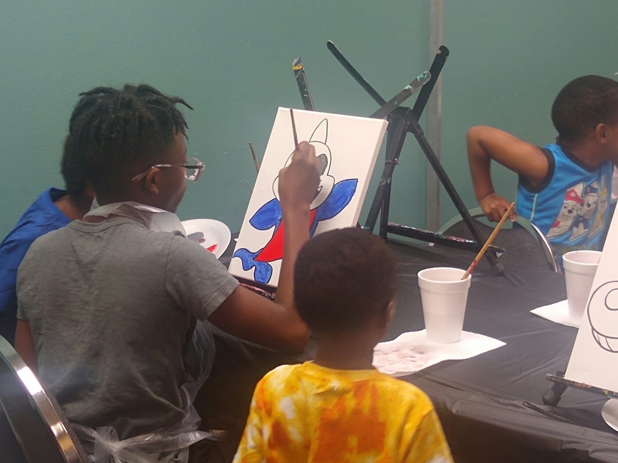 Children painting cartoons on canvases at a table.