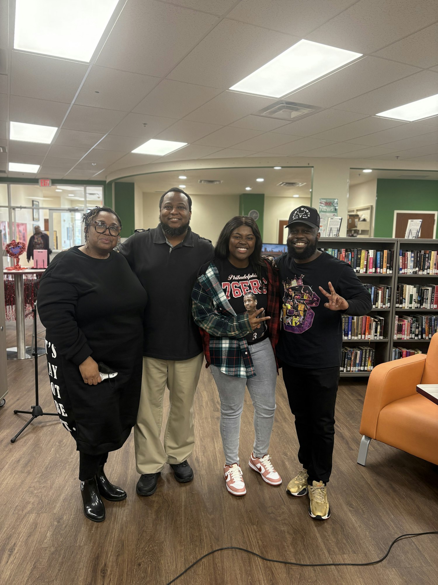 Four people posing and smiling in a library setting, books visible in the background.