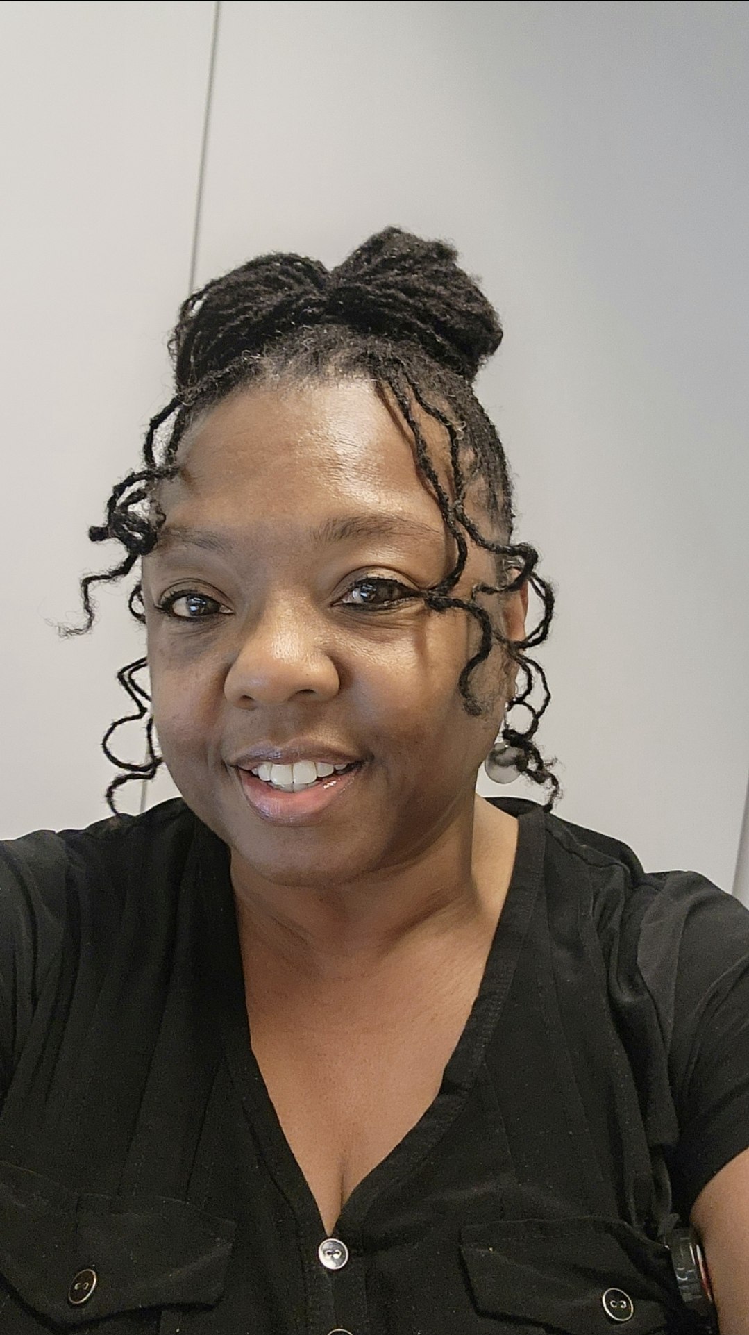 A person smiling, wearing a black shirt, with styled hair.