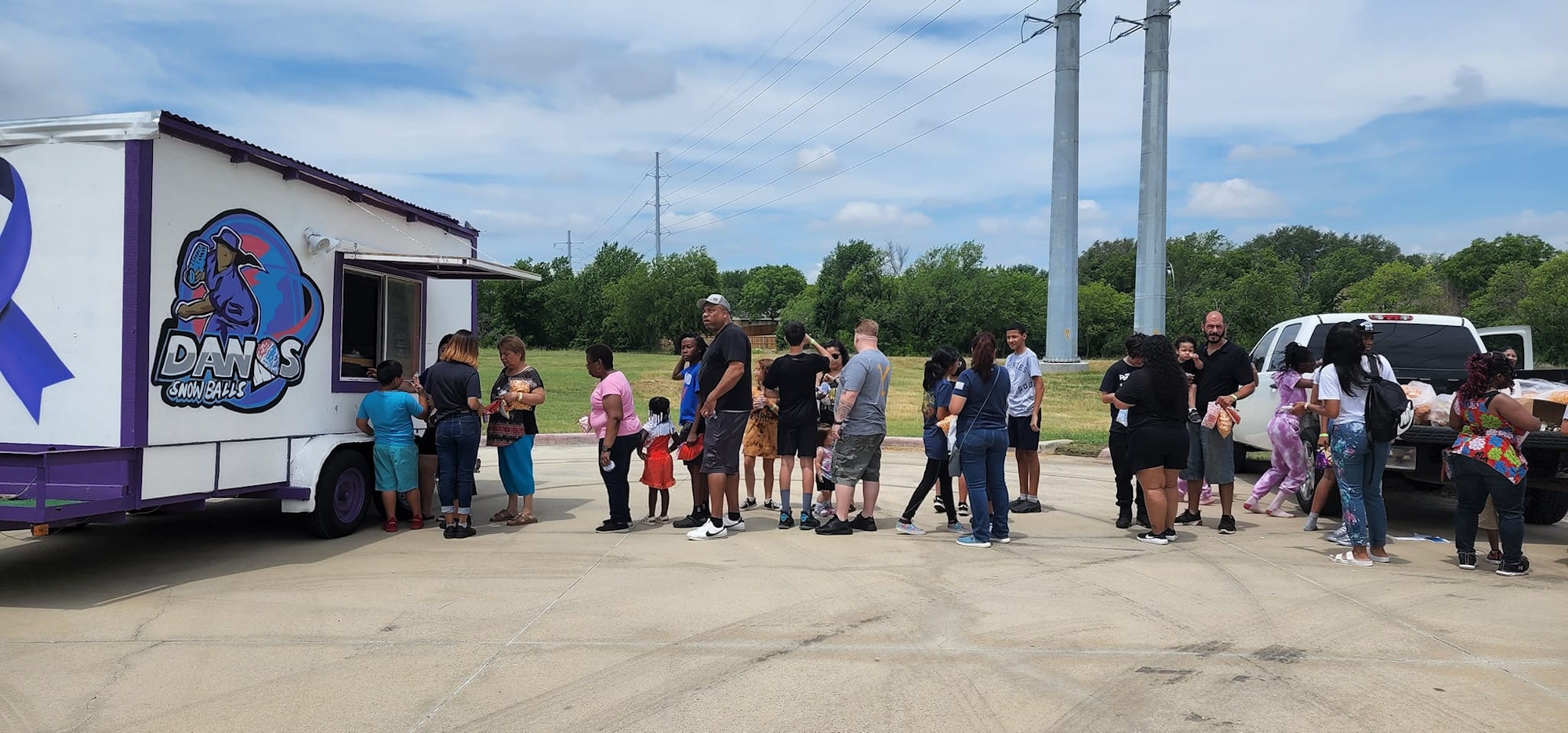 People lined up at a snowball food truck outdoors, with a truck in the background.