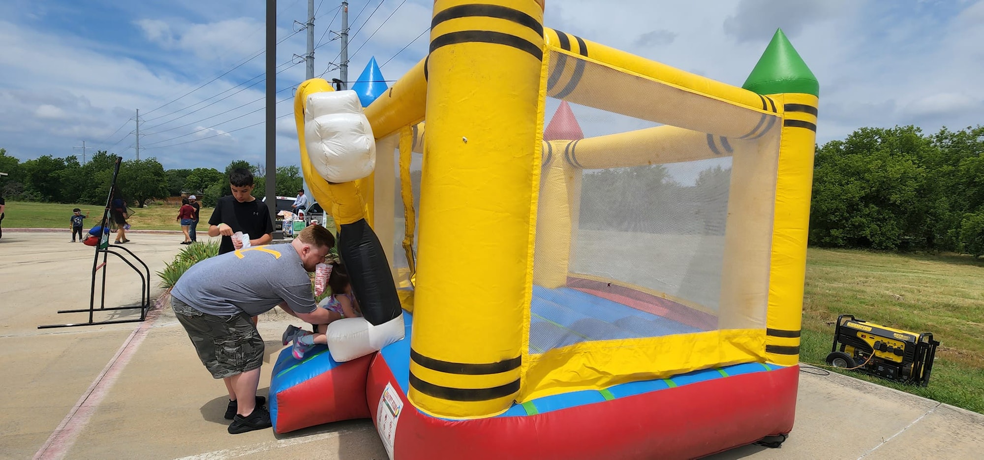 A person helping a child enter a colorful inflatable bounce house outdoors.