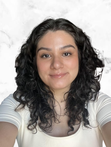 A person with long curly hair and wearing a light-colored top, smiling in front of a white background.