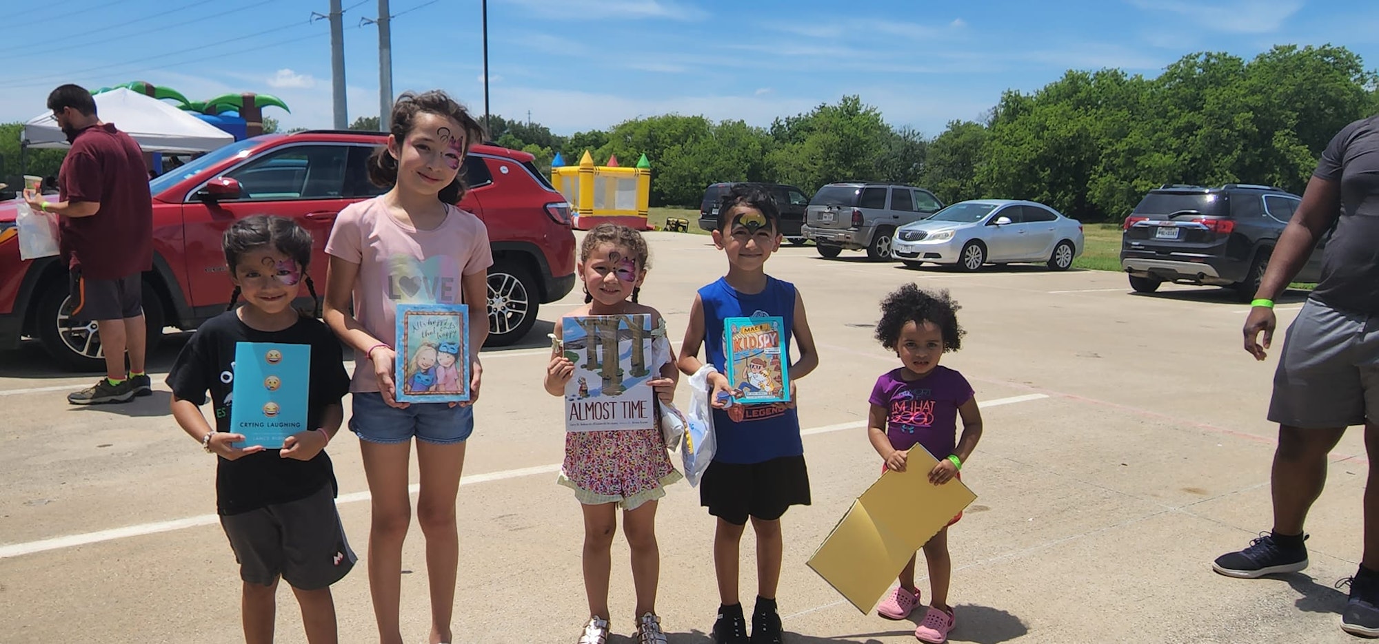 Kids with face paint holding books outdoors in a parking lot.