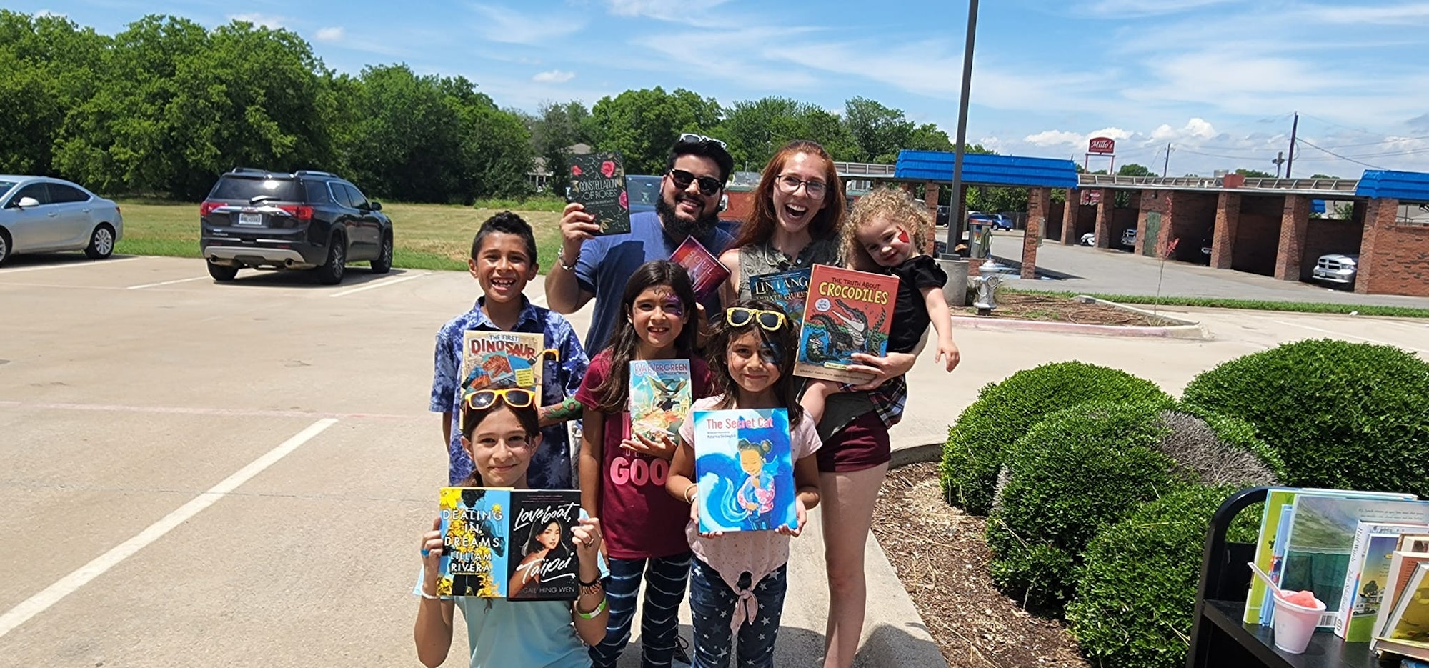 A group of people outdoors, smiling and holding various books.