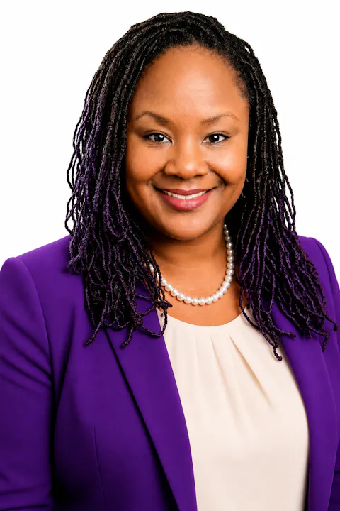 The image shows a woman with long, purple-highlighted hair, wearing a purple blazer and a pearl necklace, smiling warmly.