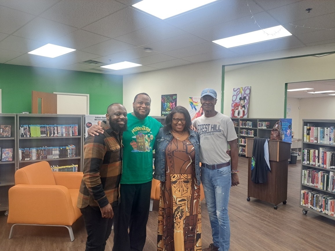 Four people smiling in a room with bookshelves and orange chairs.
