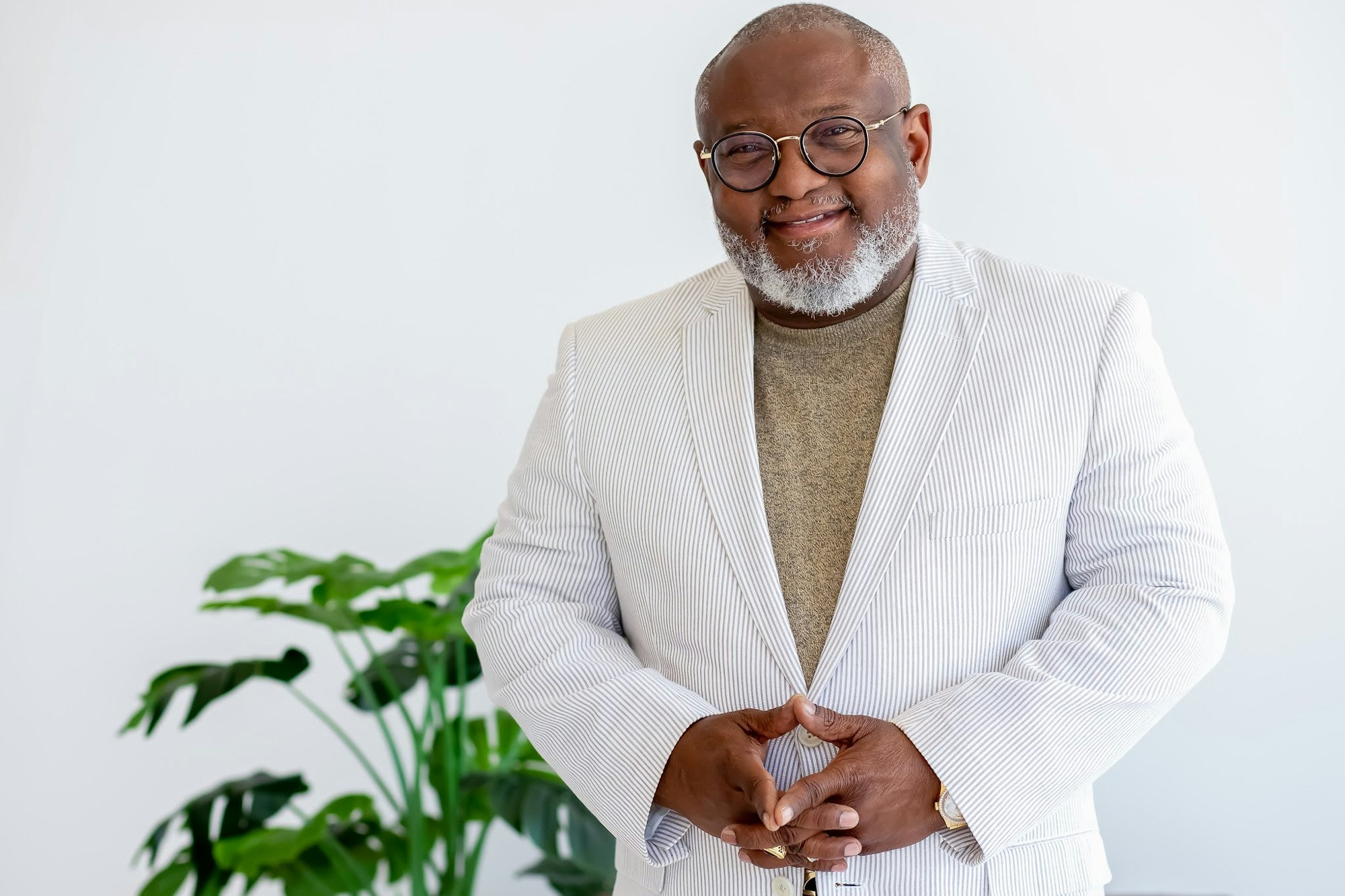 Smiling man in a white striped suit jacket, standing in front of a plant.