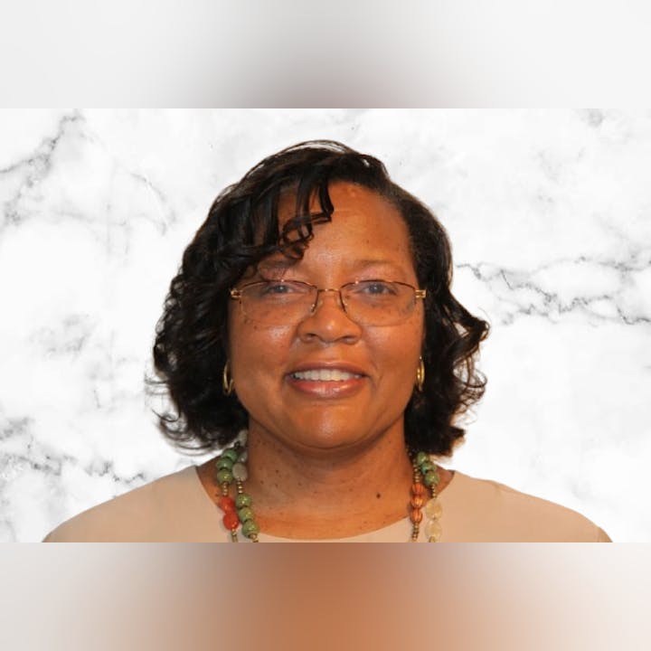 A person smiling, wearing glasses, a necklace, and earrings, with a marble textured background.