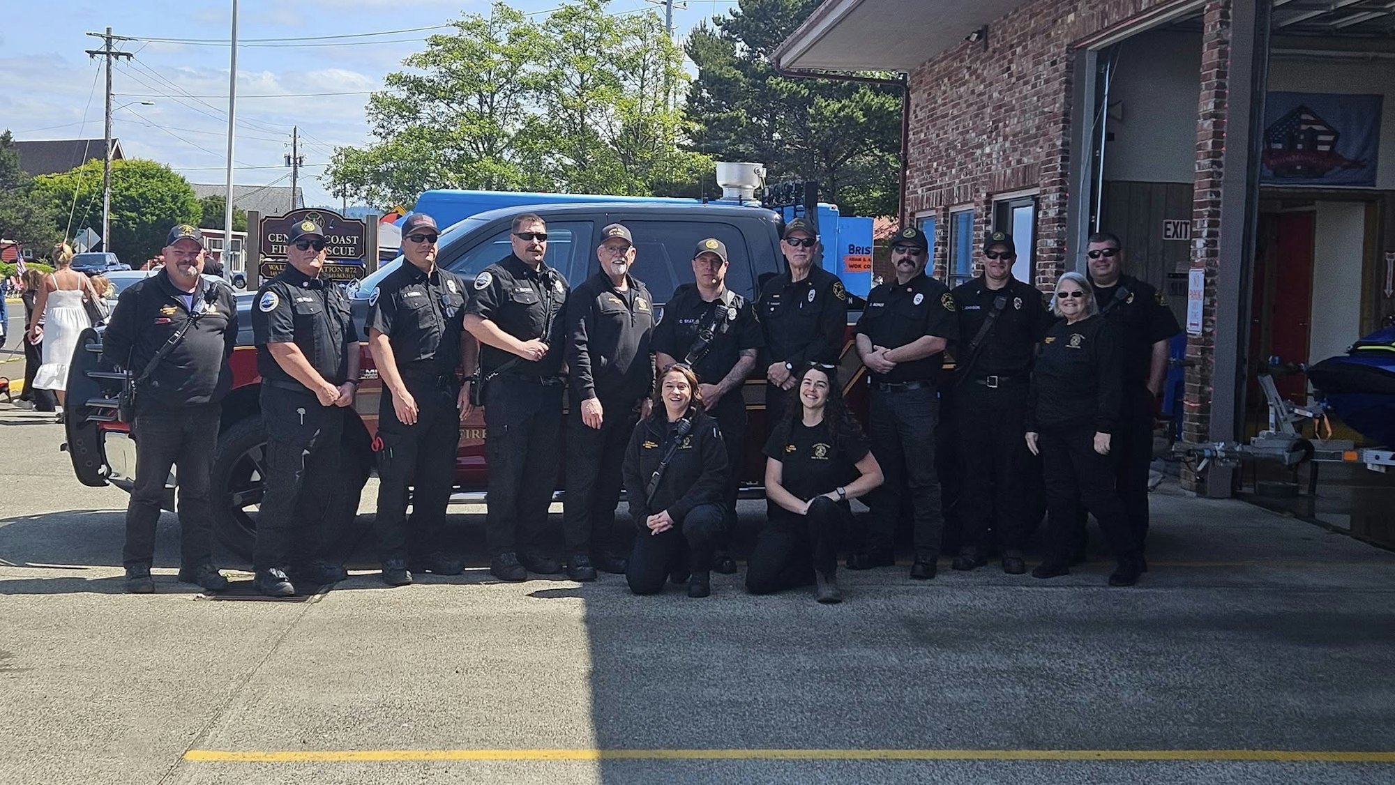 A group of uniformed individuals posing in front of a vehicle outside a building with signage in the background.