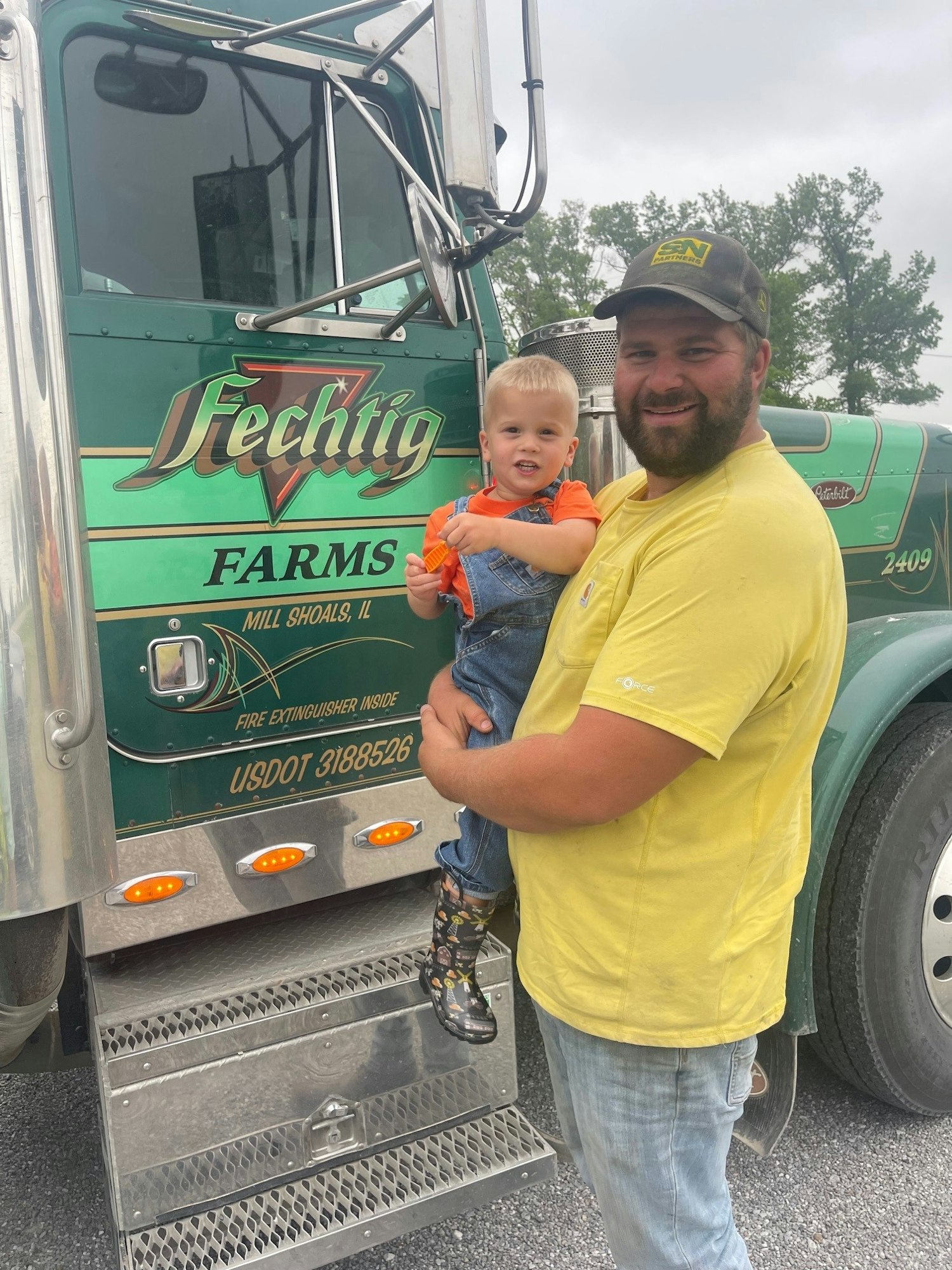 Cole Fechtig holding son Lane by Fechtig Farms truck.
