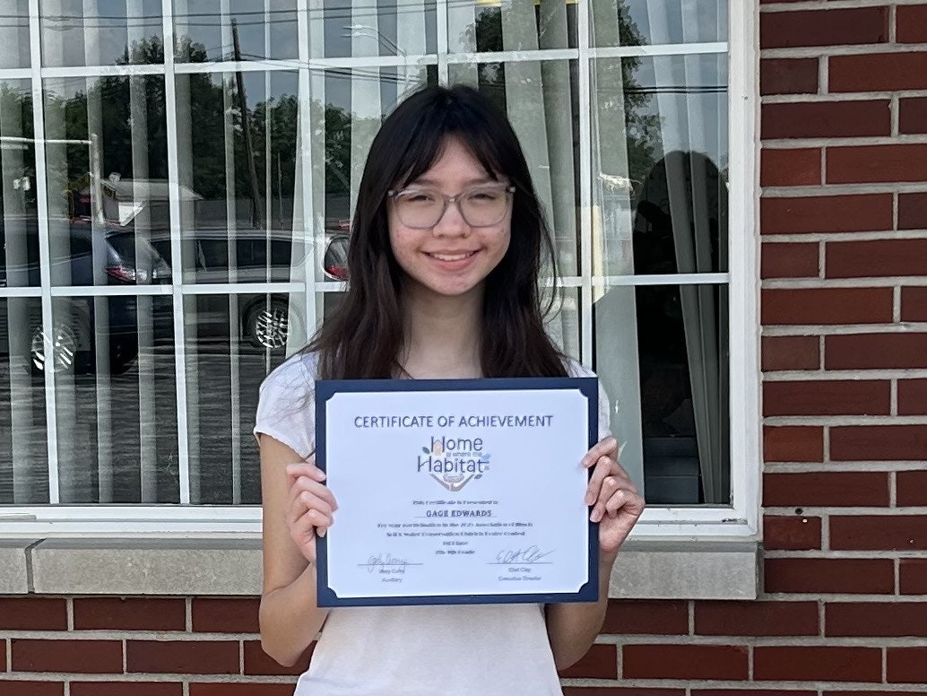 A person holding a certificate of achievement in front of a brick building with a window.