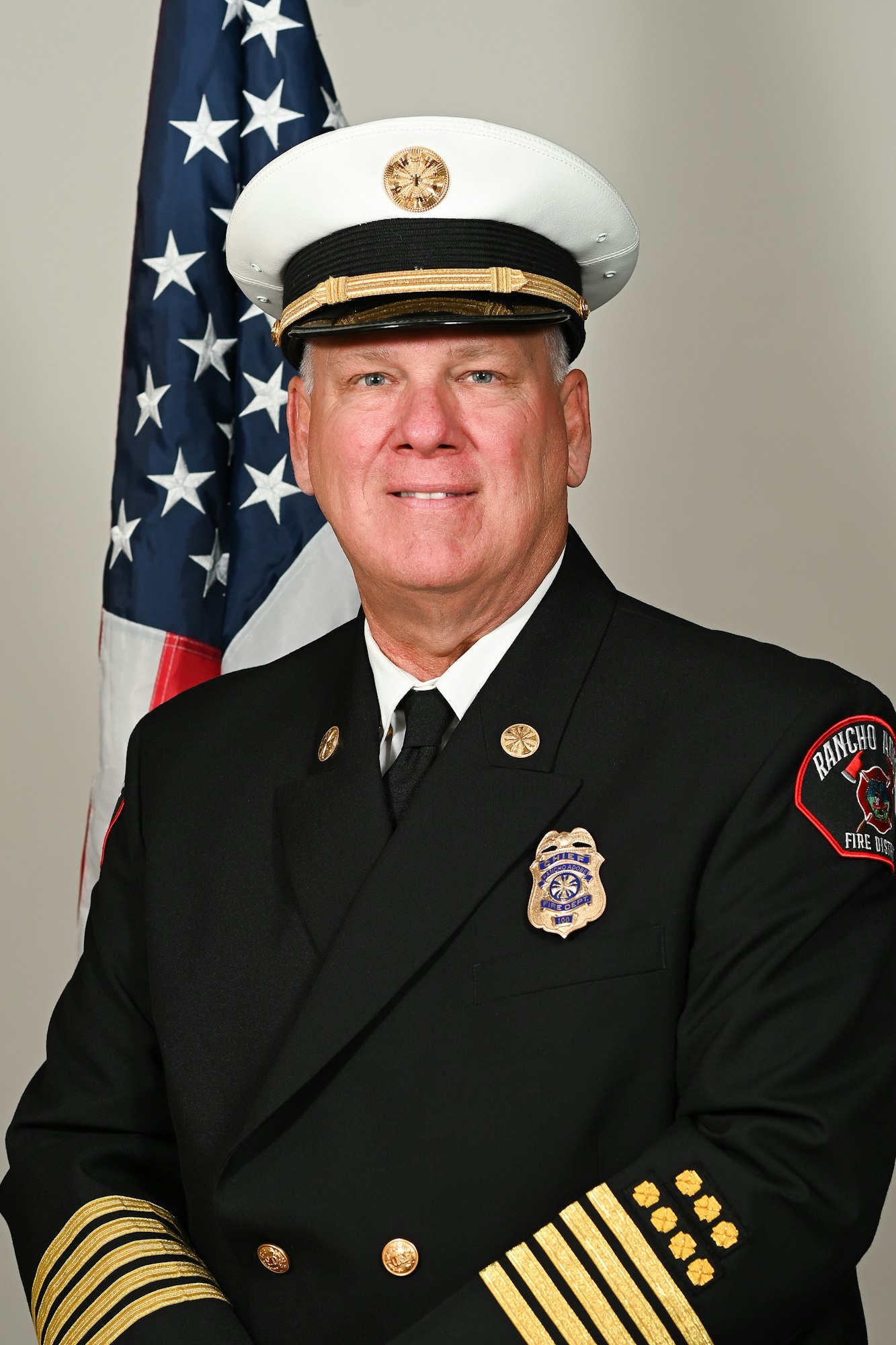 A firefighter in a formal uniform with an American flag in the background.