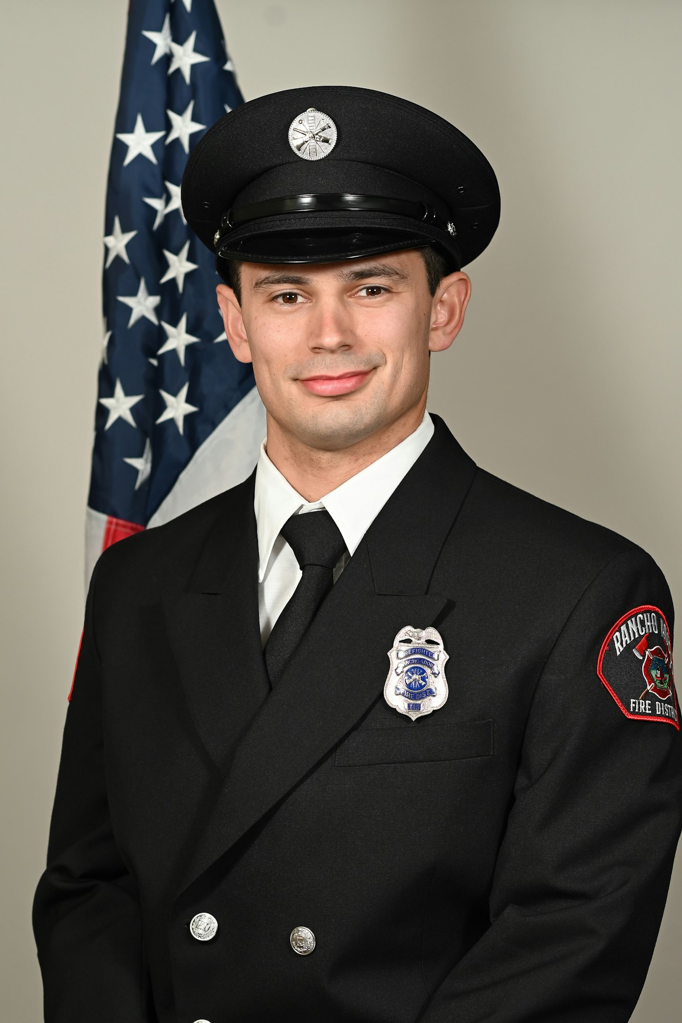 A firefighter in uniform with badges, in front of the American flag.