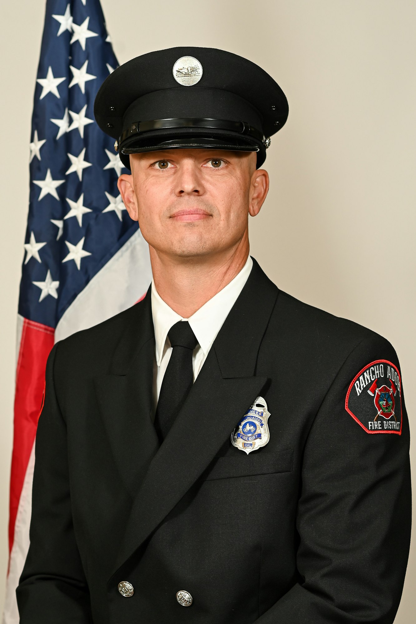 A firefighter in uniform stands in front of a U.S. flag.
