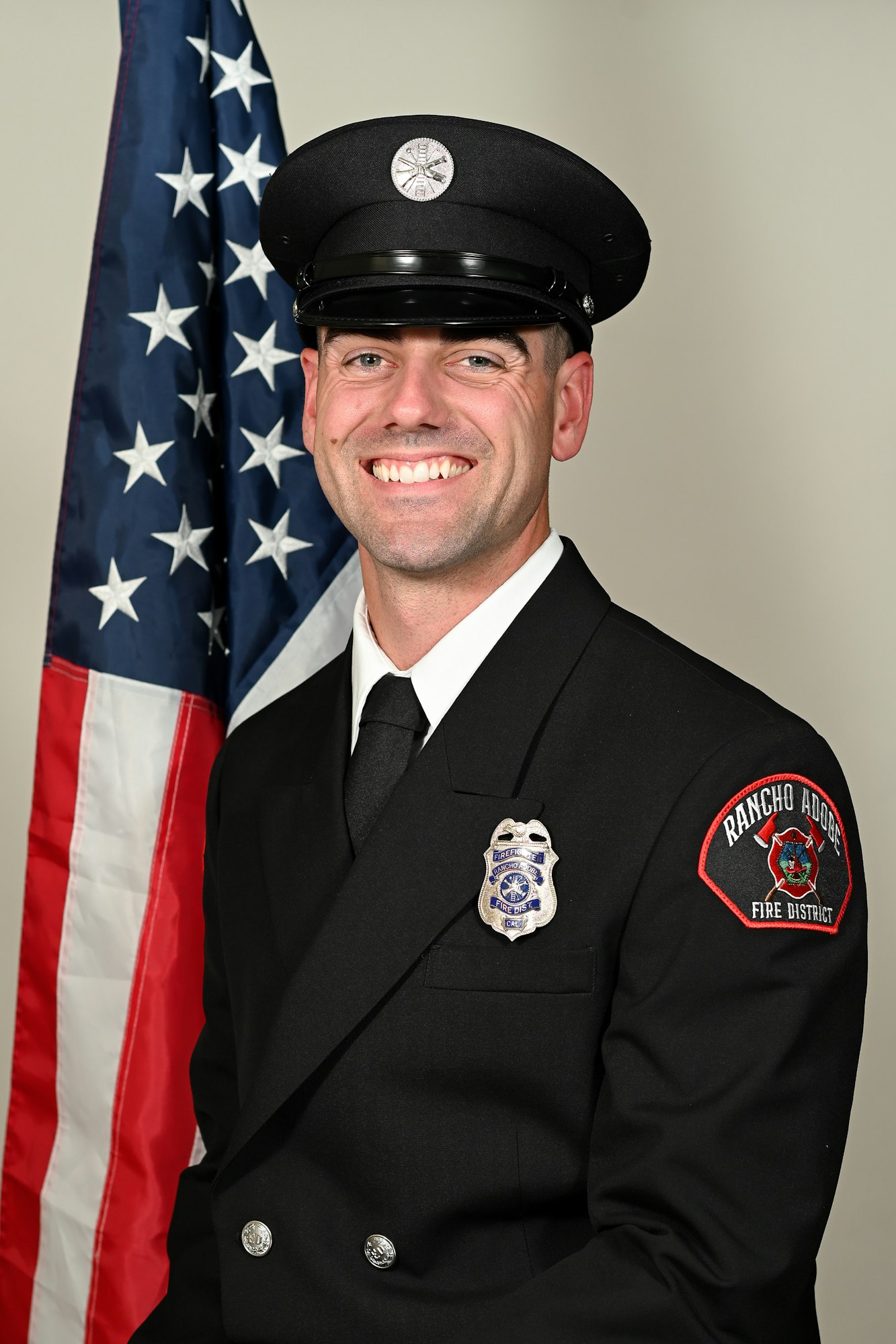 A smiling firefighter in uniform stands in front of an American flag.