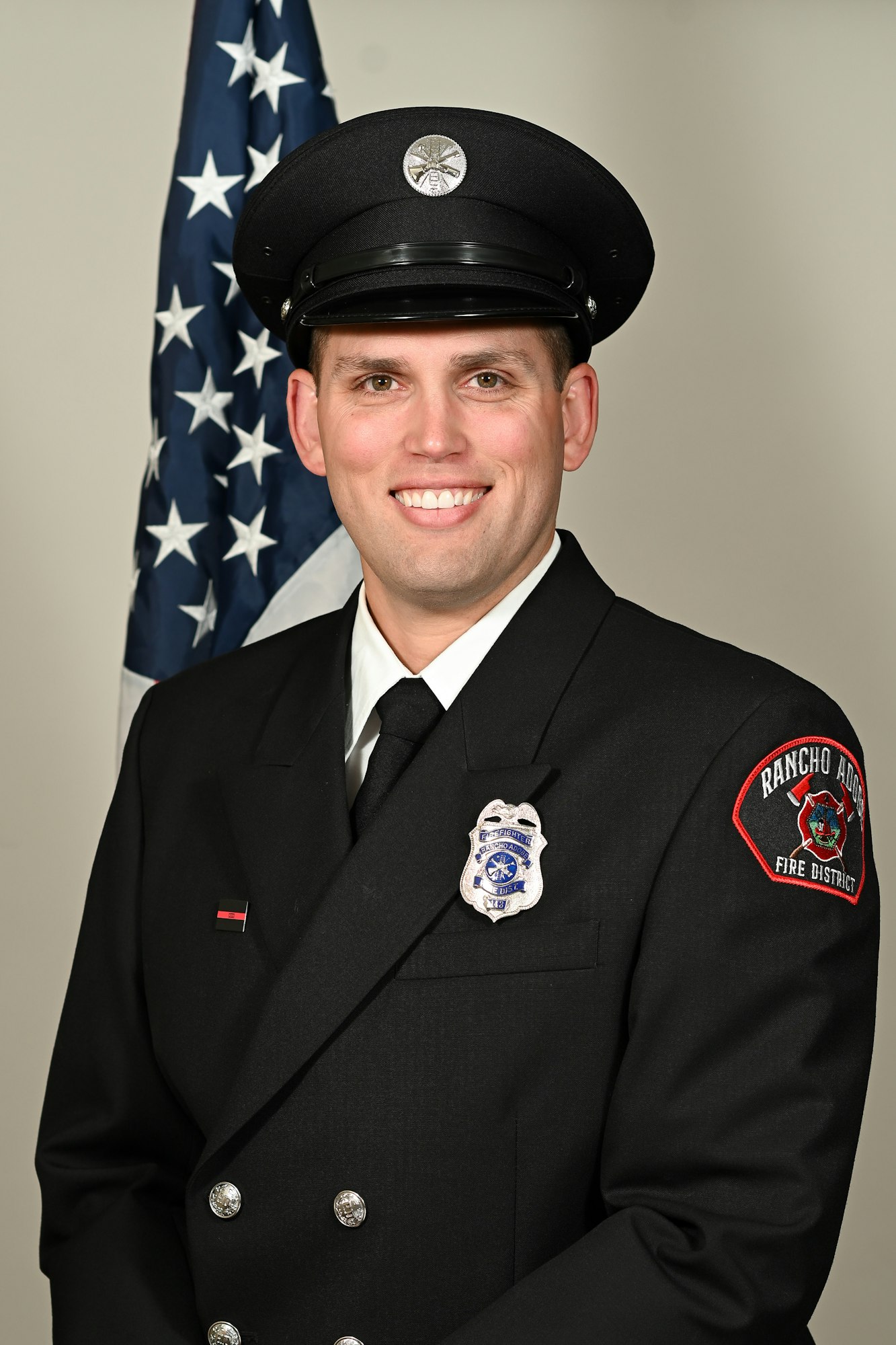 A firefighter in uniform, smiling, standing in front of an American flag.