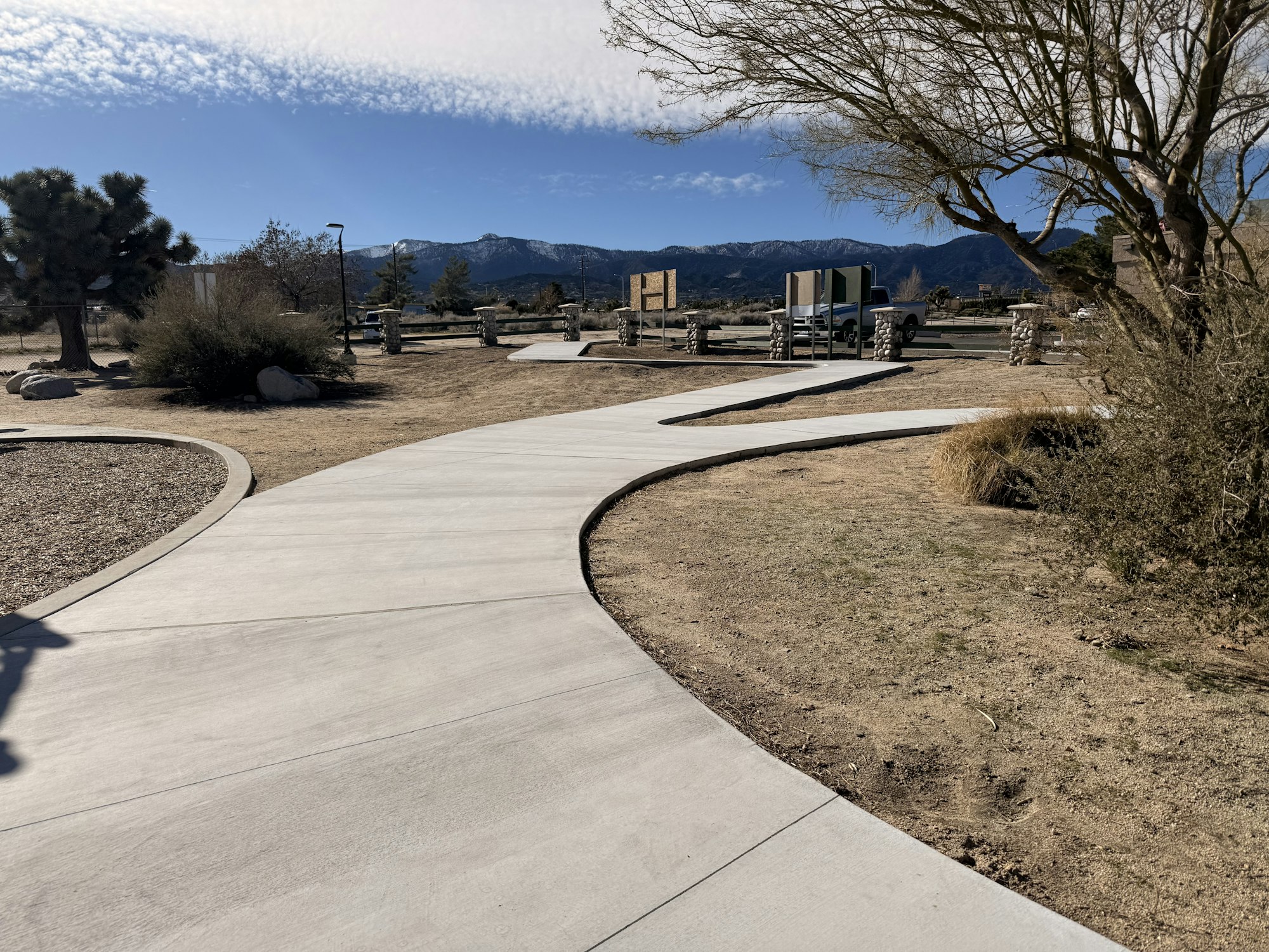 A winding walkway in a sunny outdoor park with mountains in the background, surrounded by sparse vegetation.