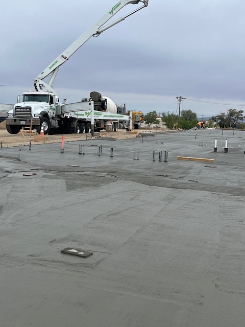 A construction site with a concrete mixer truck pouring cement on a freshly laid concrete surface and scaffolding nearby.