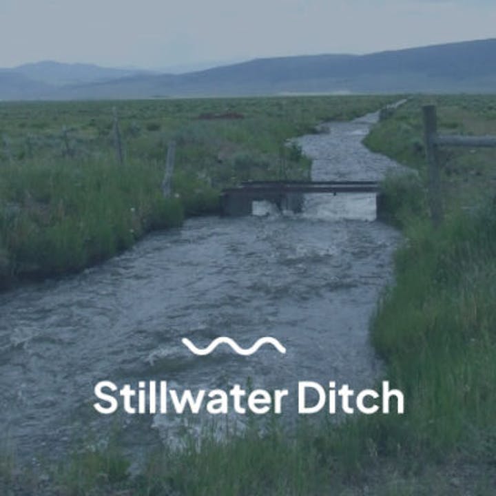 A flowing ditch in a grassy field, labeled "Stillwater Ditch," with mountains in the background.