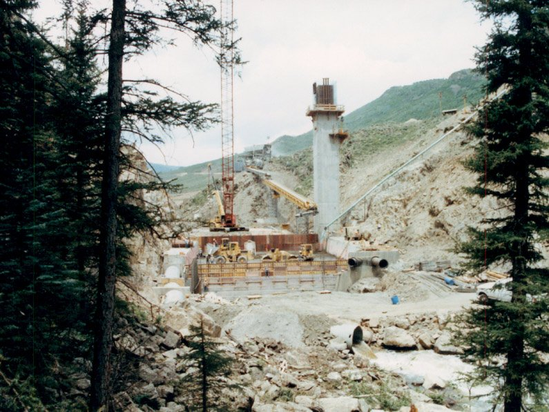 A construction site with cranes, machinery, and a concrete structure surrounded by trees and hills.